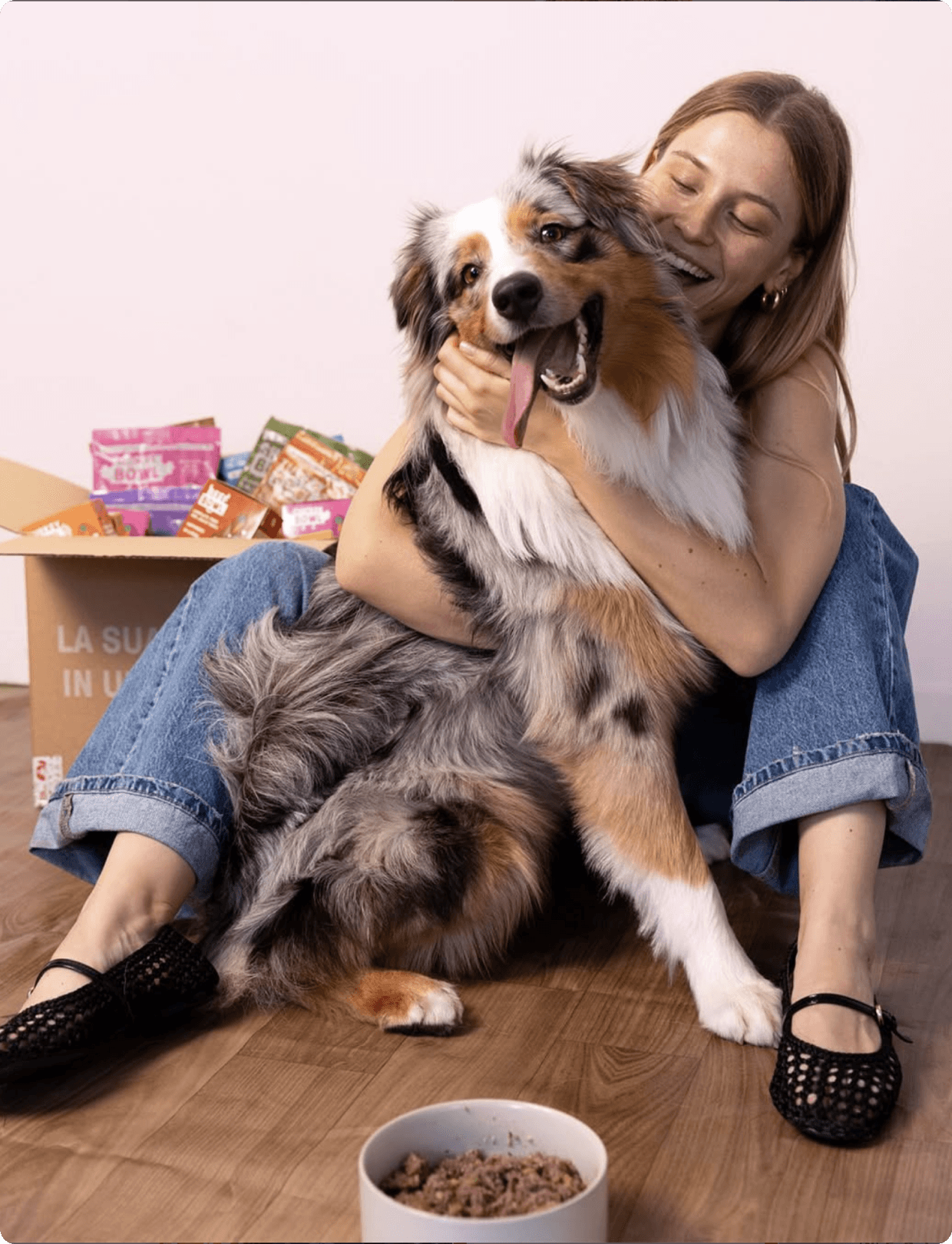 A woman hugging her dog with a Dog Heroes box behind them
