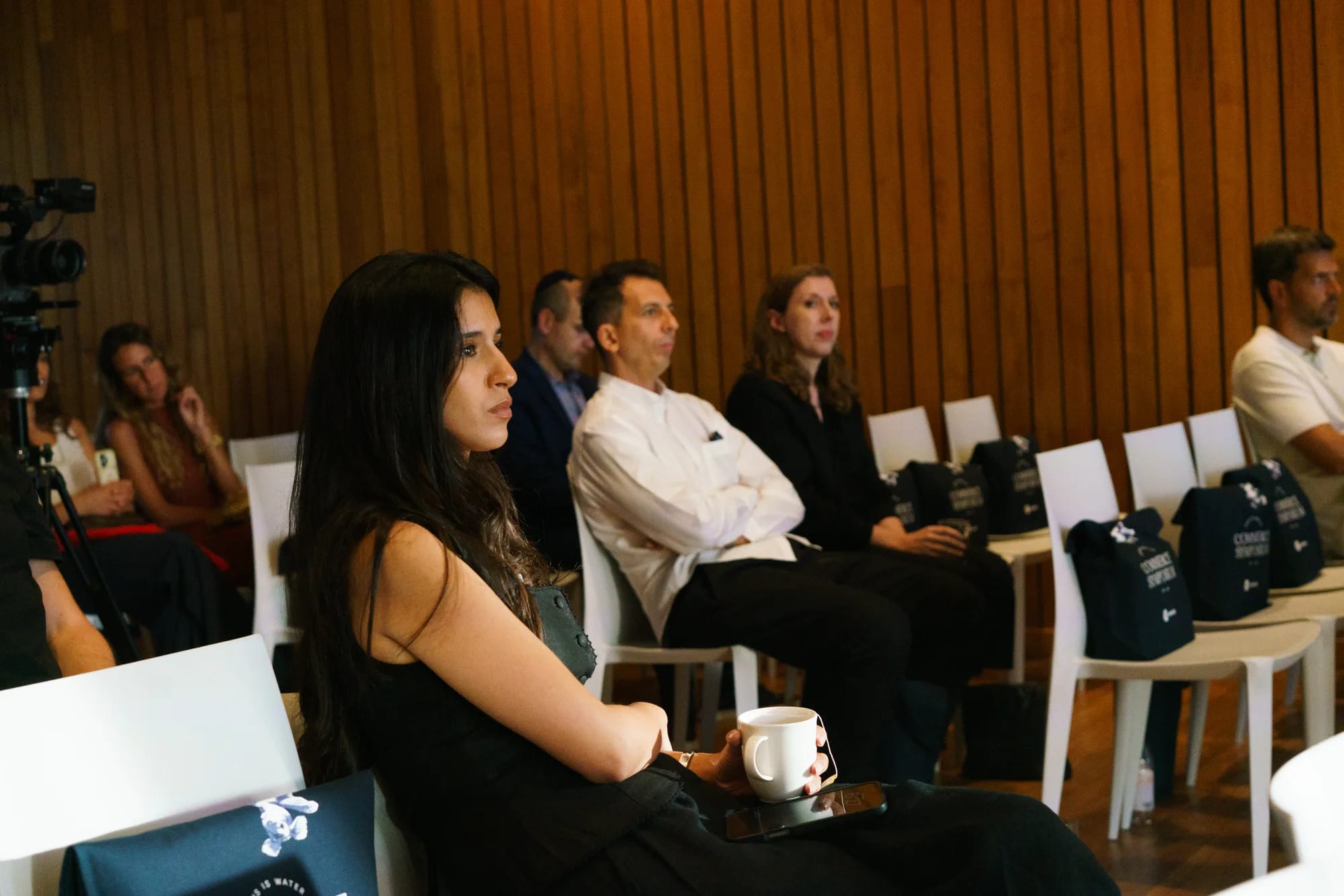 Audience members listen from rows of white chairs holding event tote bags