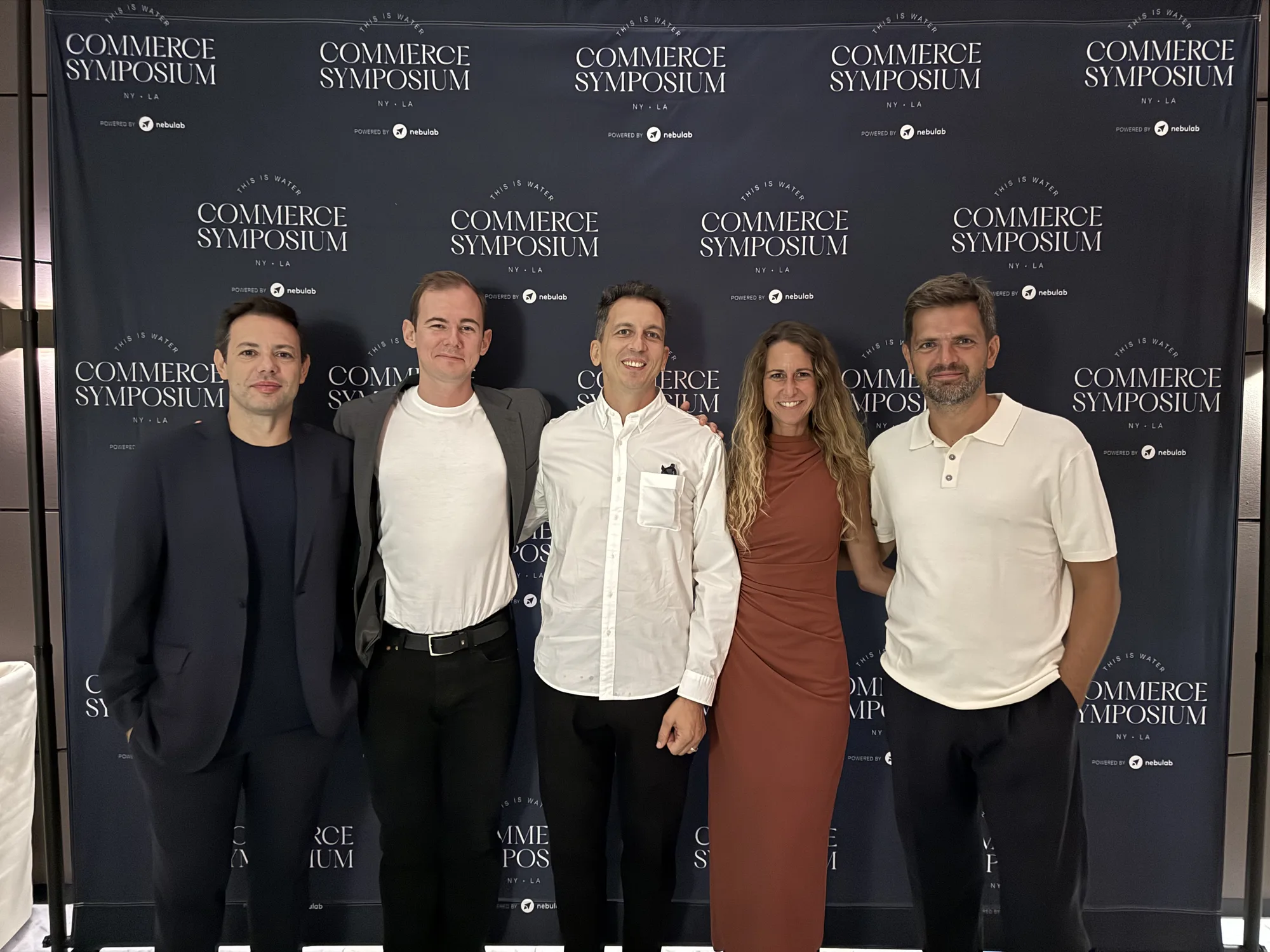 Five people pose together in front of the Commerce Symposium backdrop