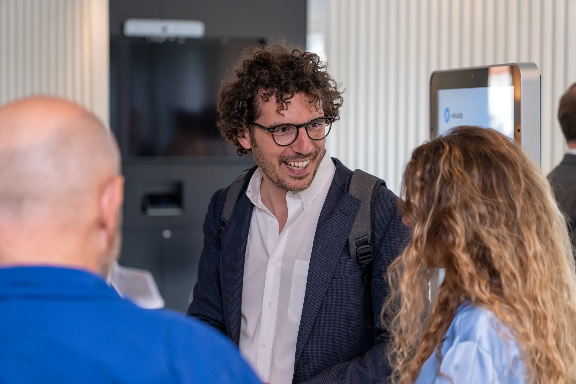 A guest in glasses and a blazer laughs while chatting with two others on arrival