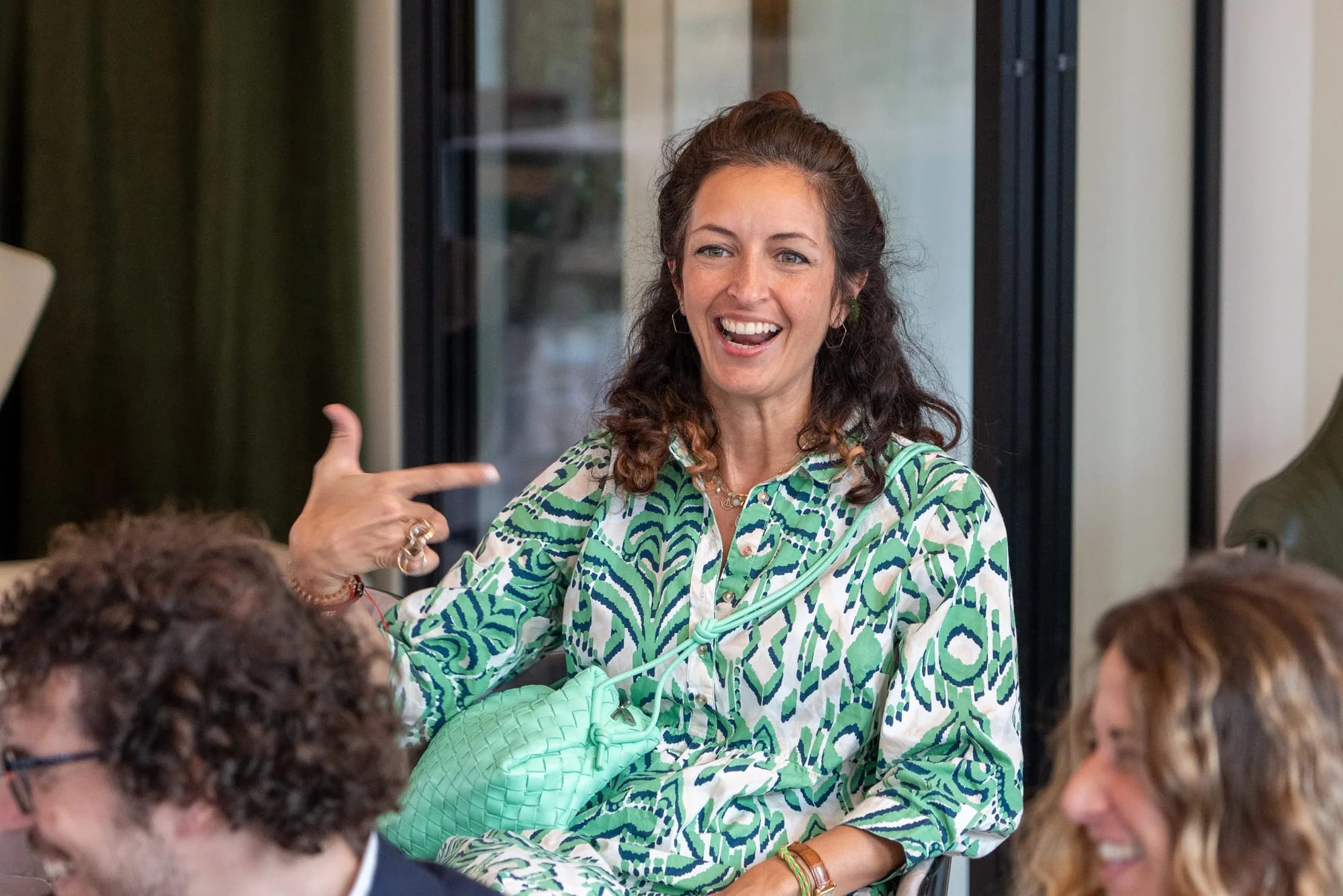A guest in a green patterned dress laughs and points during the conversation