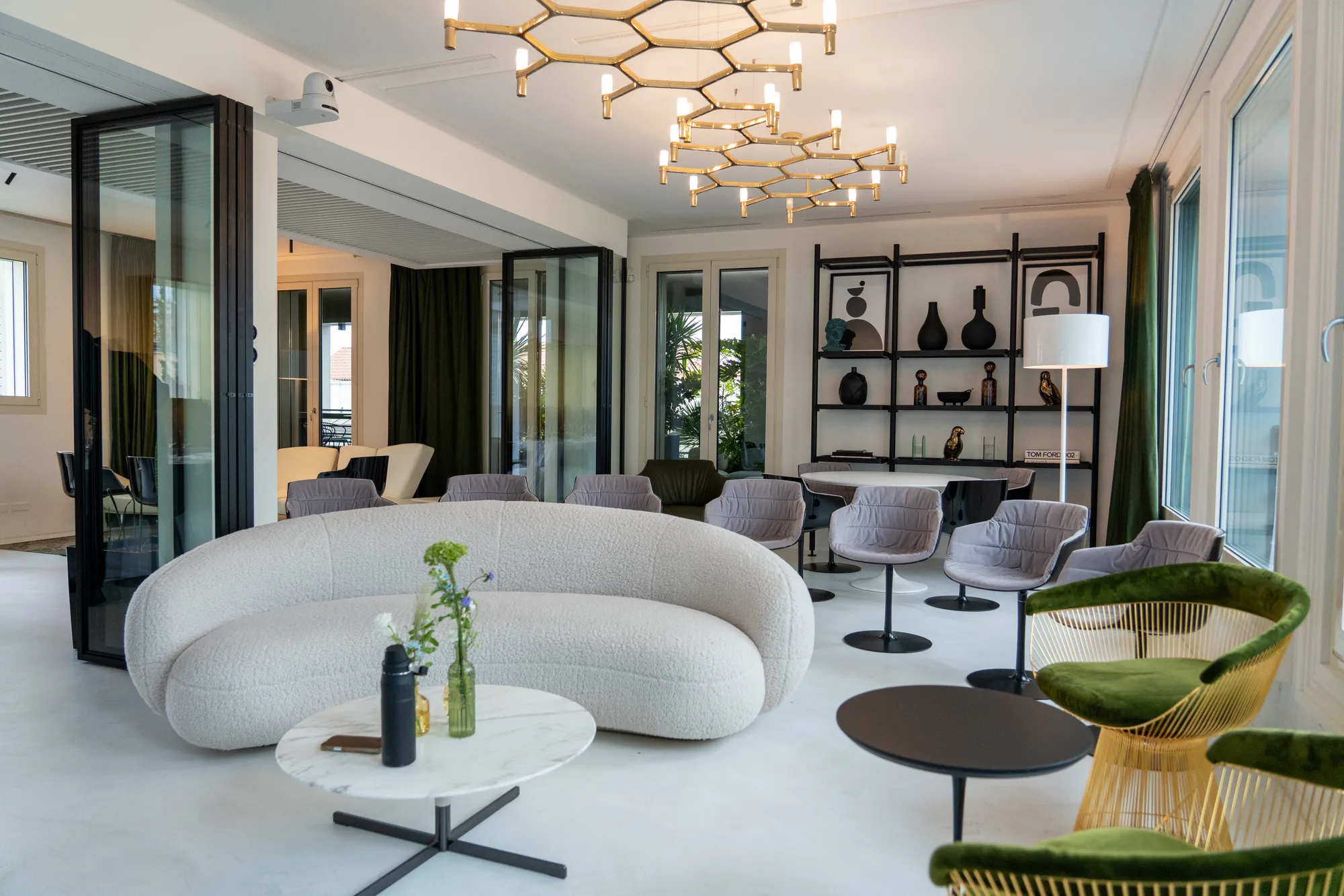 A bright lounge with a curved bouclé sofa, swivel chairs and gold honeycomb chandeliers