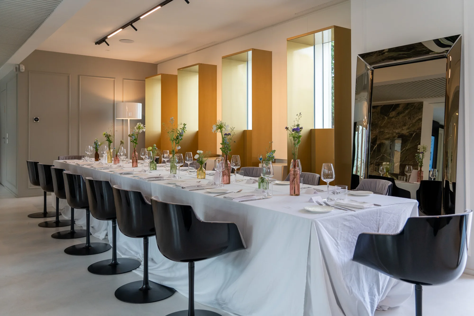 A long dinner table laid with white linen, glassware and flowers in coloured bottles