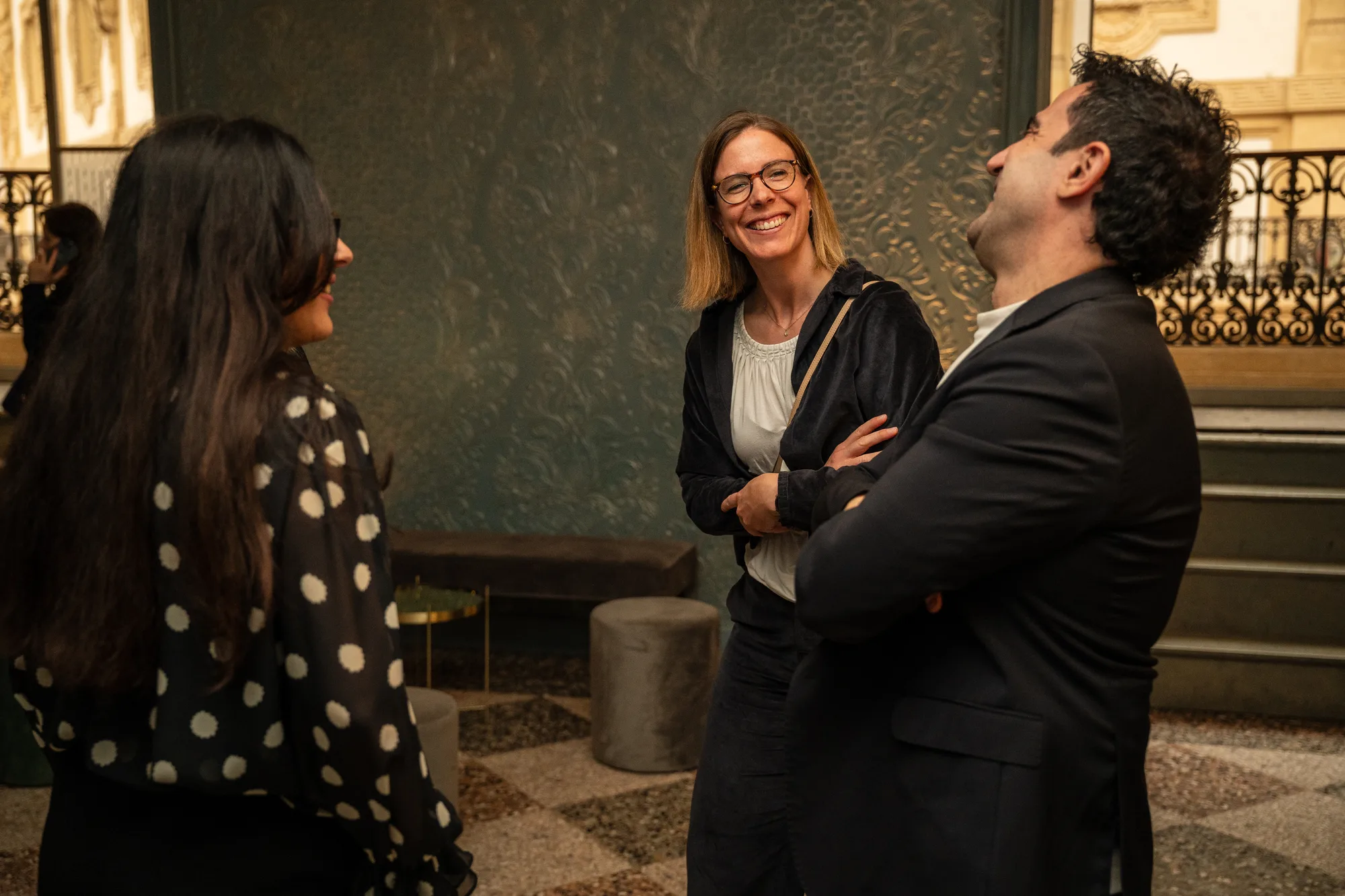 Three guests laughing together in the lounge by a wrought-iron balcony