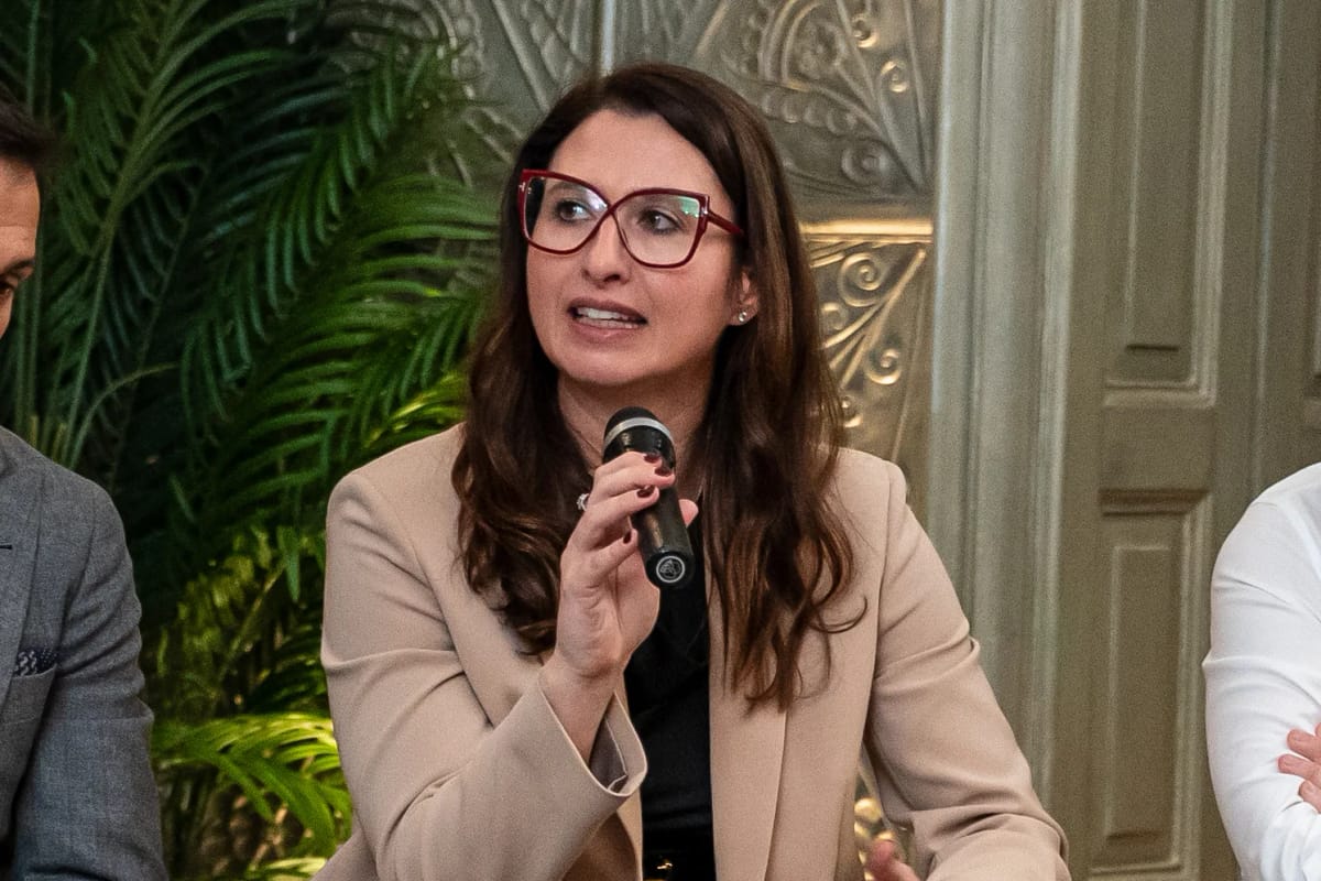 Panelist in a beige blazer speaking into a microphone during a roundtable