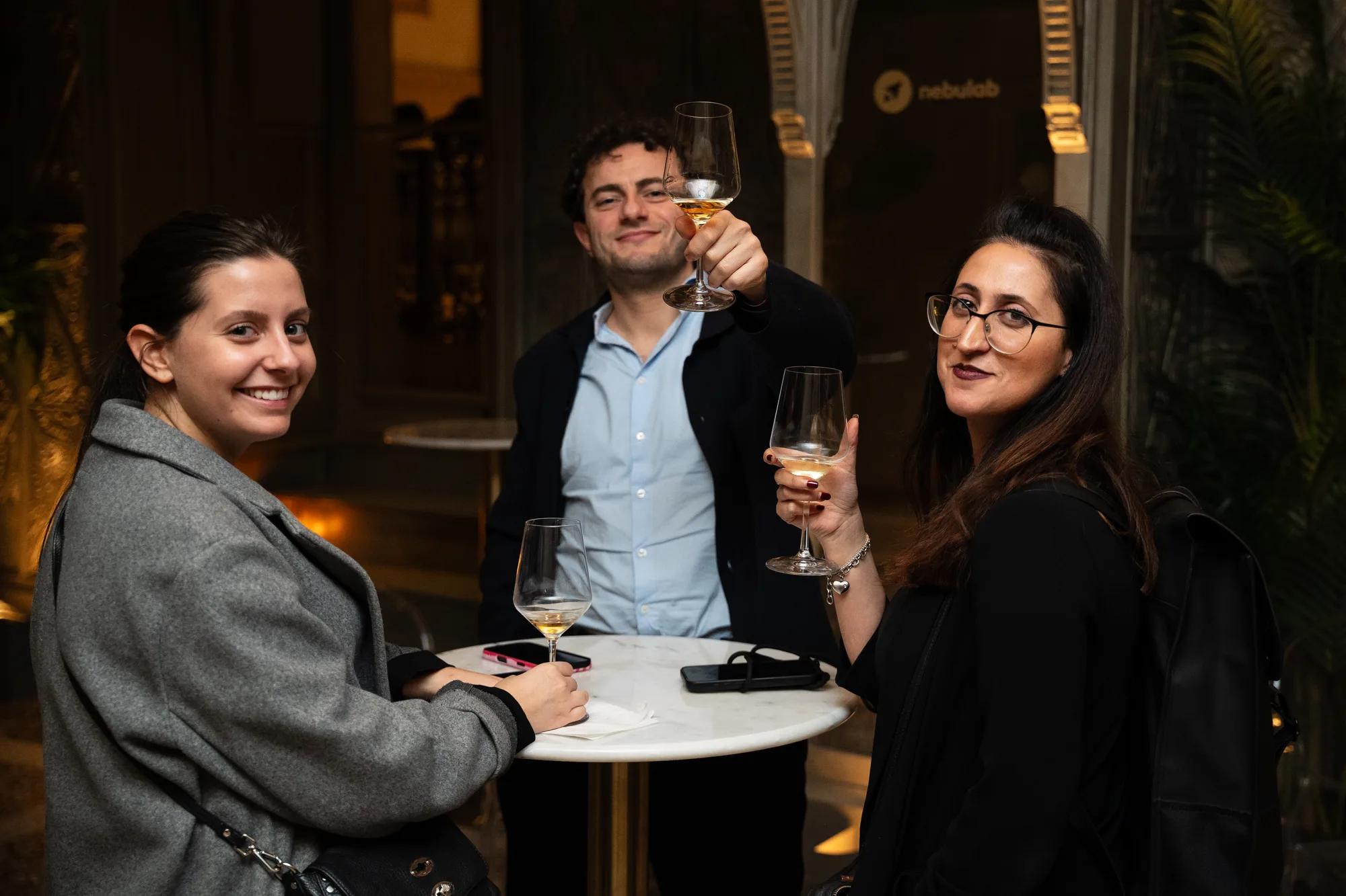 Three guests raising glasses of wine at a marble table during the aperitivo