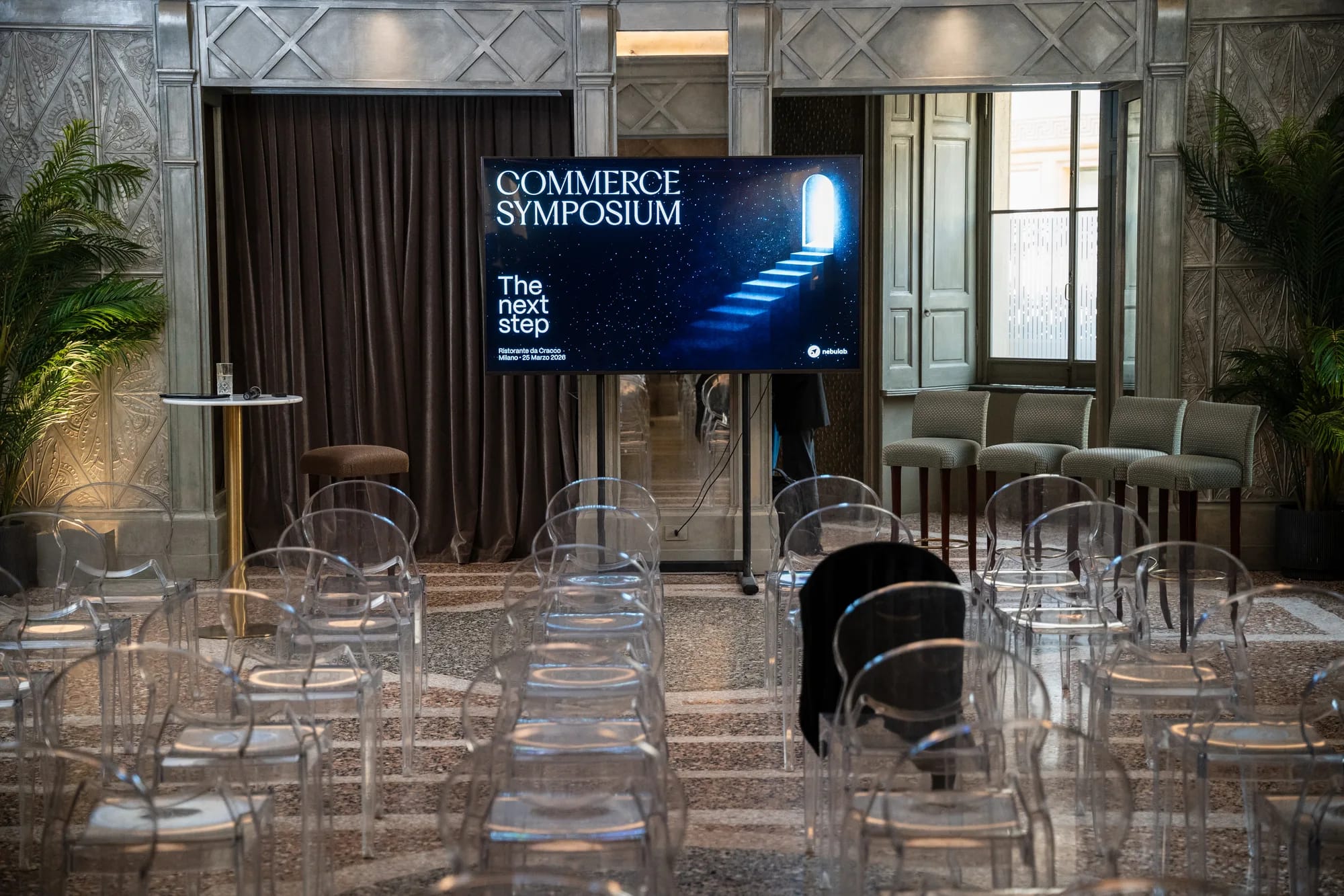 Rows of clear chairs facing a screen showing the Commerce Symposium title slide