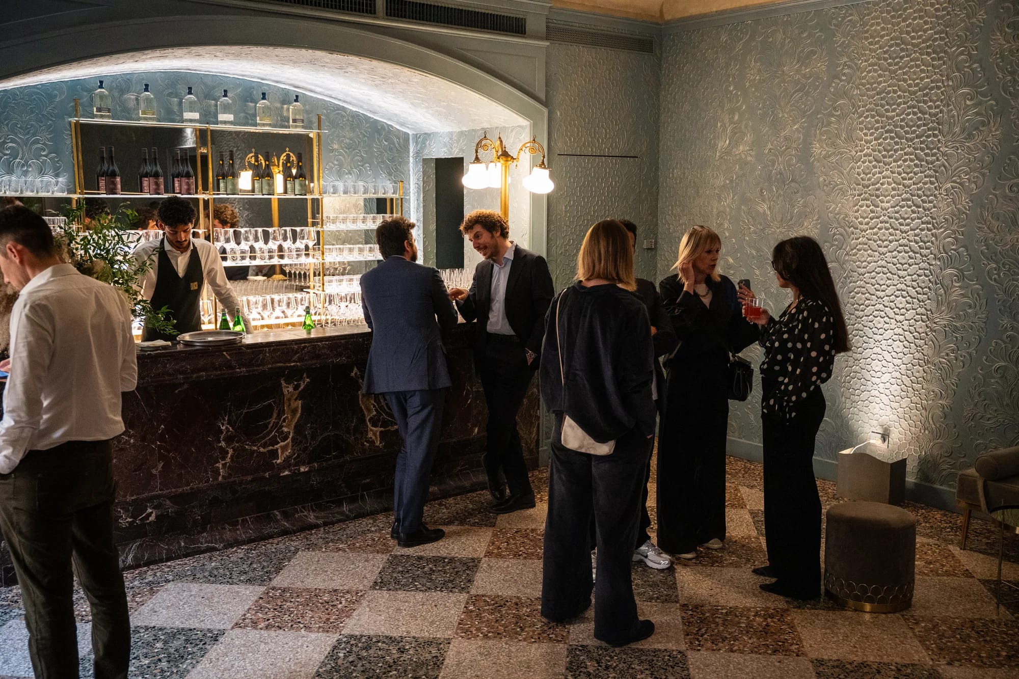 Marble bar under a vaulted ceiling with guests mingling on a checkered floor