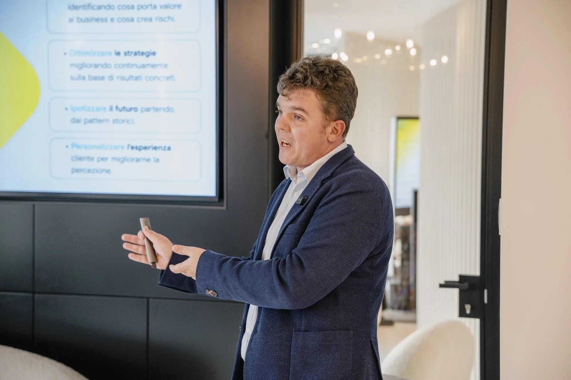 A speaker gestures with a clicker while presenting a slide in Italian