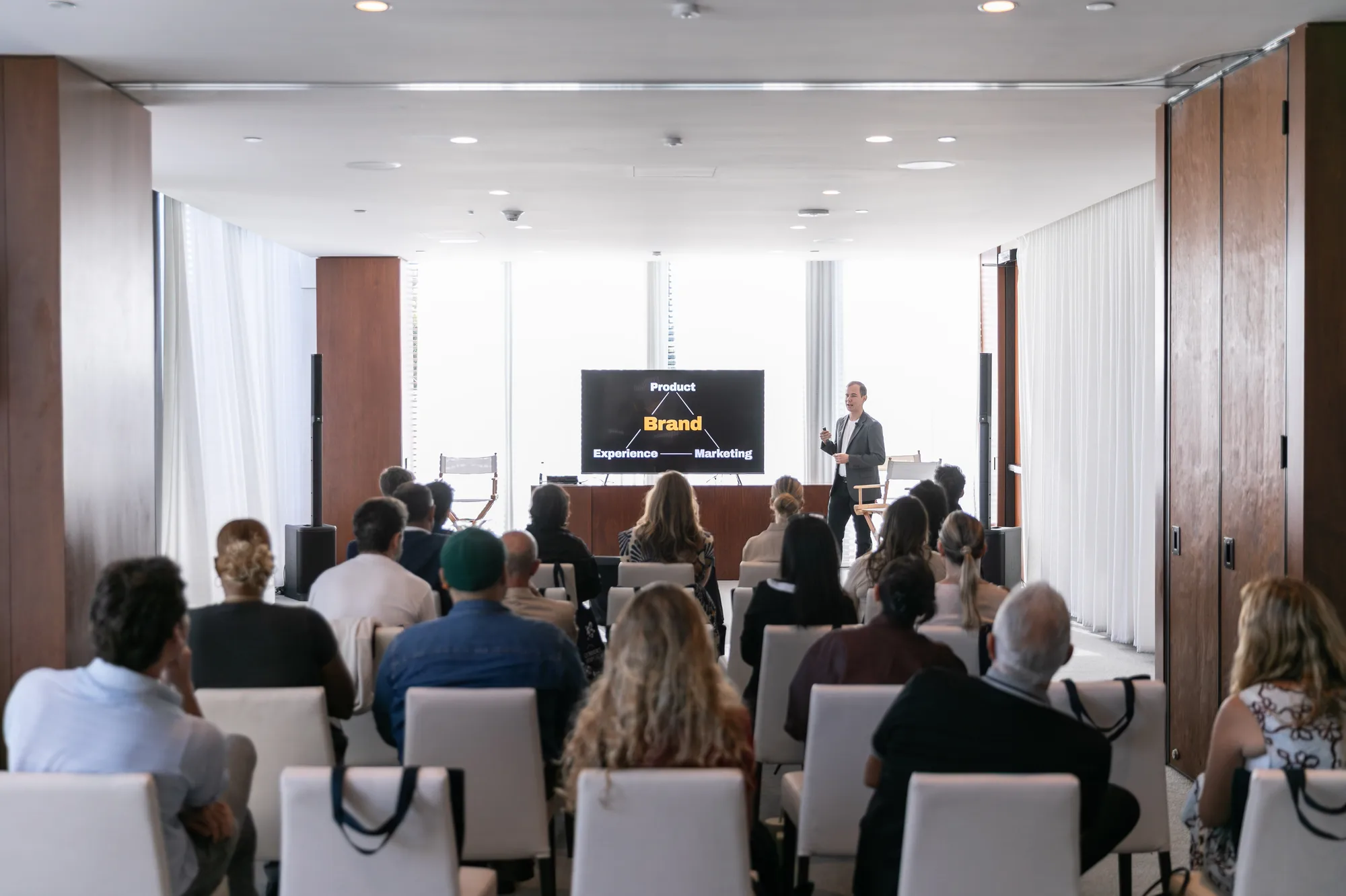 A seated audience watches a speaker present a slide about brand