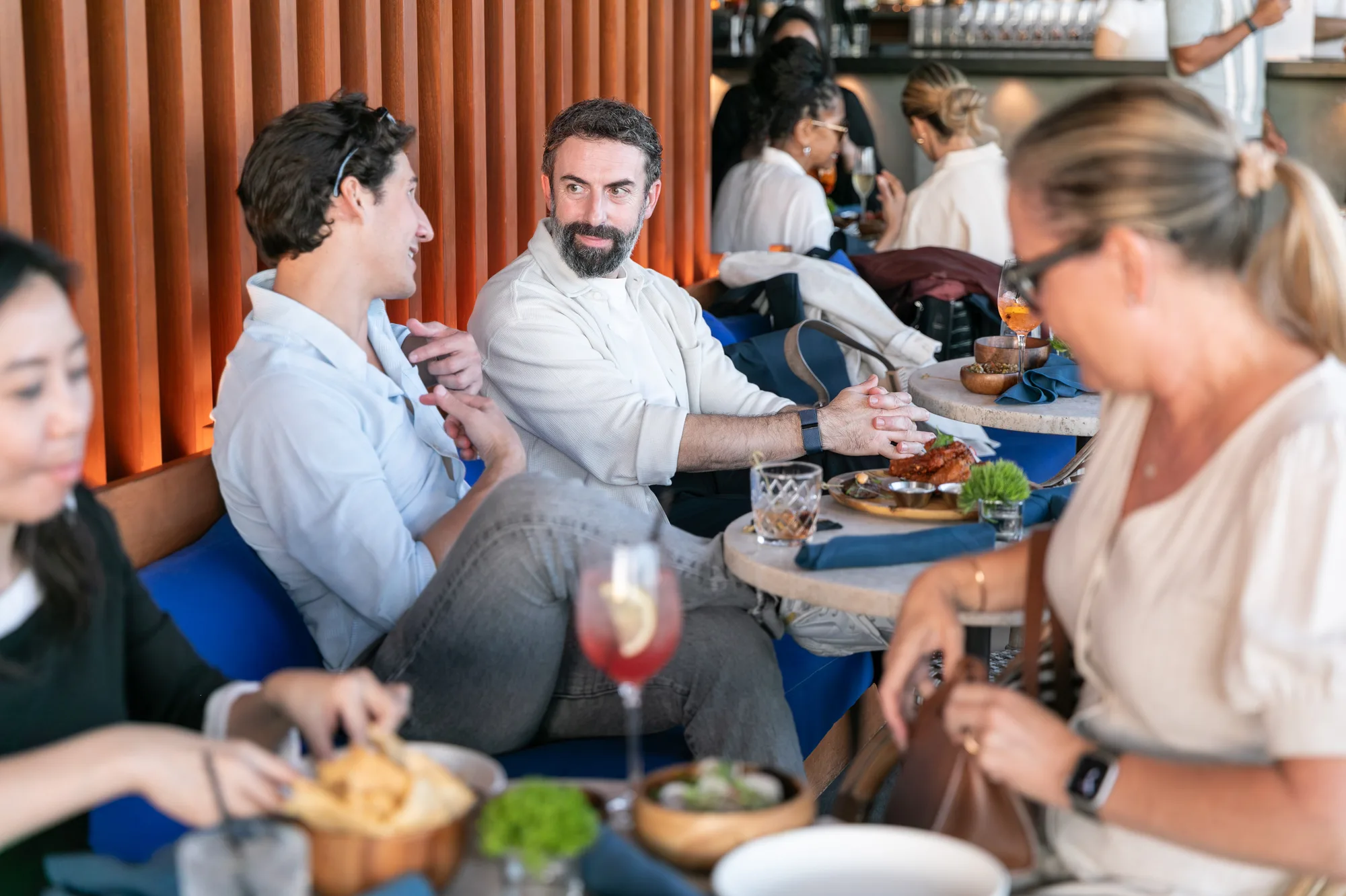 Guests sharing food and drinks on blue banquettes at the rooftop restaurant