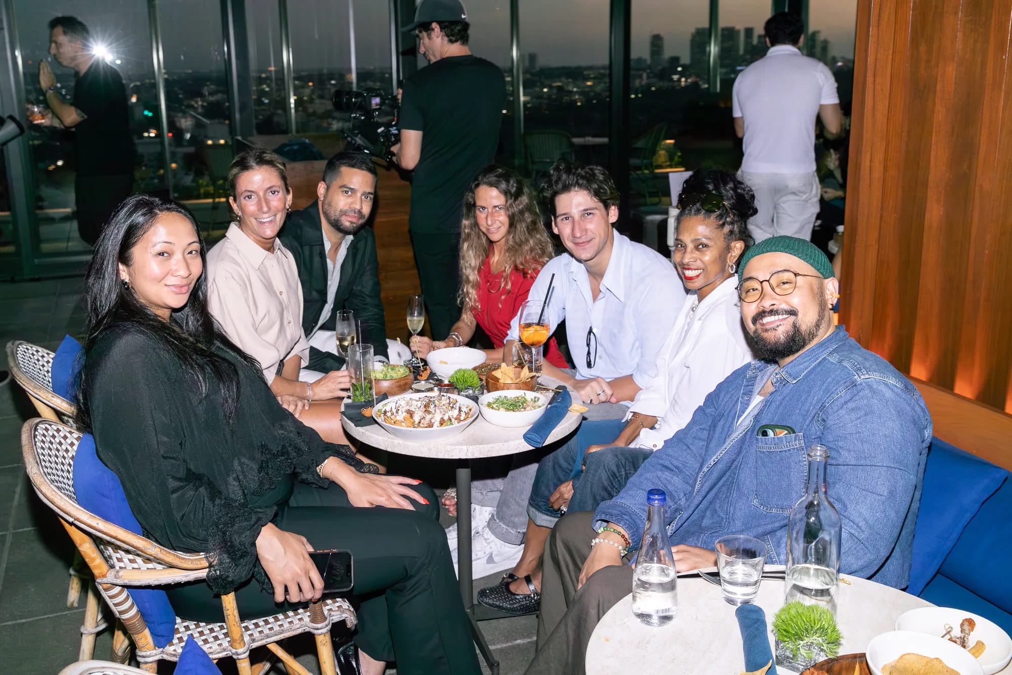 A group of guests smiling around a table on the rooftop at dusk