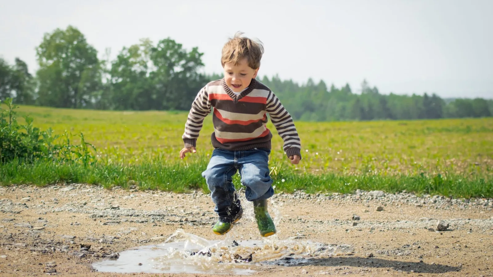 A child jumping into a puddle in a field.